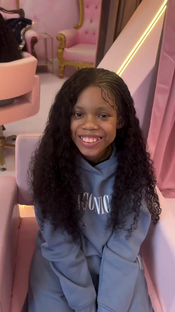 A smiling girl wearing her new long, curly Little Lady Locks wig in the pink salon